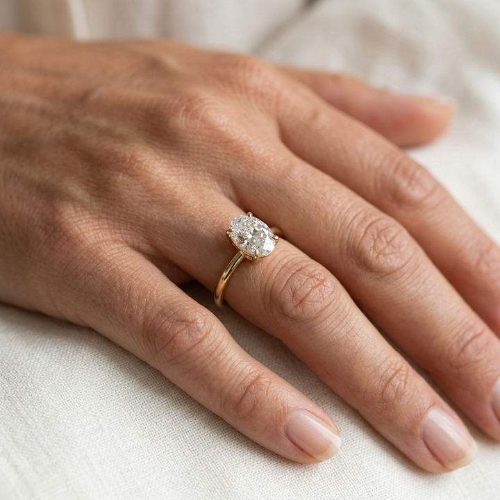 Oval diamond solitaire ring with a slim yellow gold band, shown close-up on a hand.